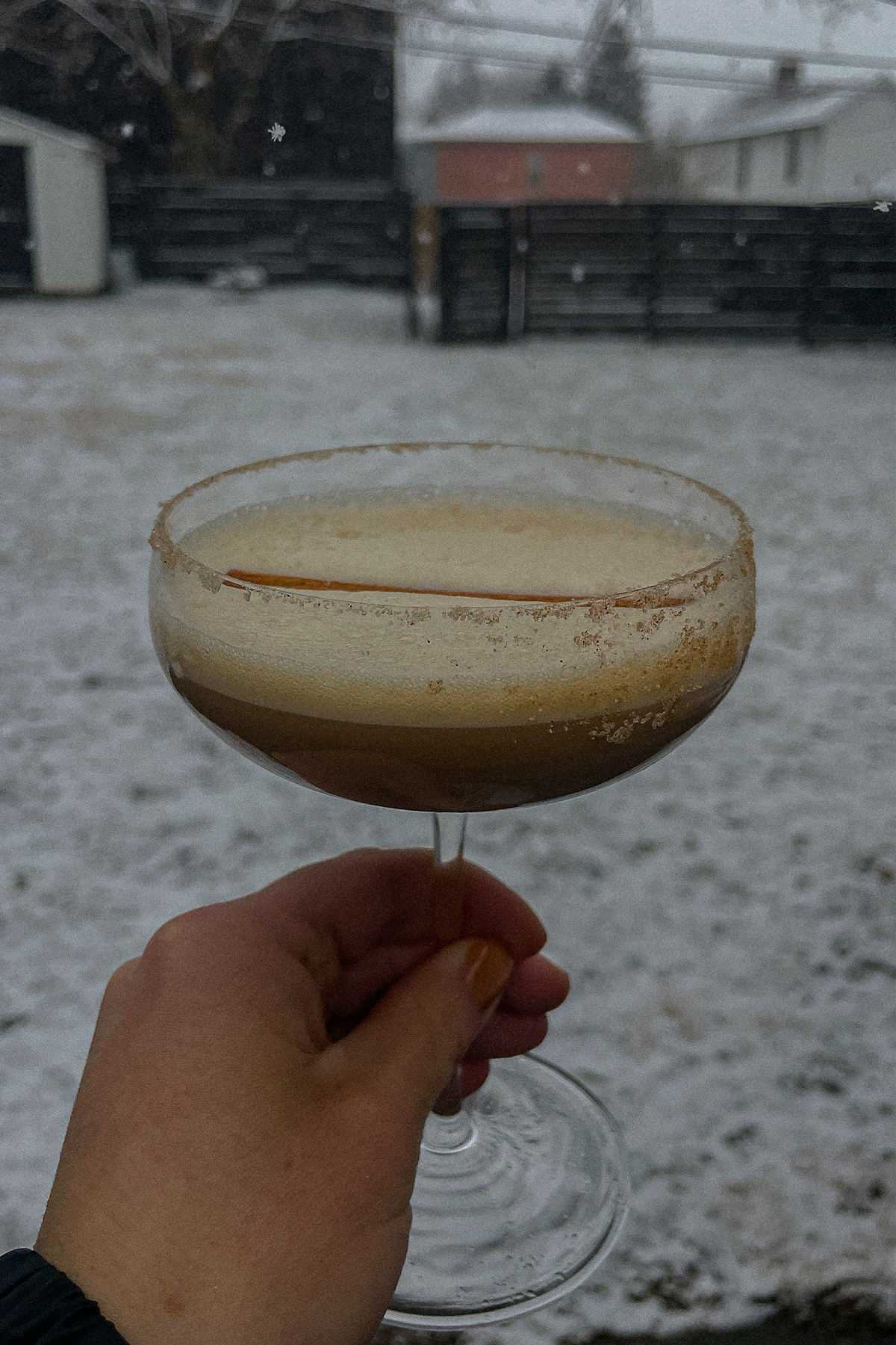 Creamy Dirty Chai Martini topped with a cinnamon stick outside with snow falling around it