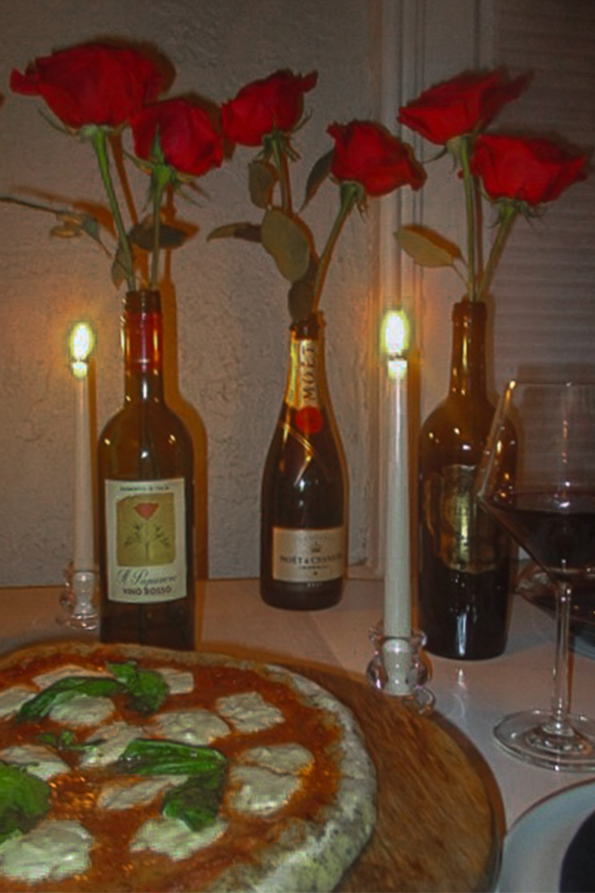 Valentine's Day dinner table with homemade pizza, red wine glass, candles and red rose arrangement