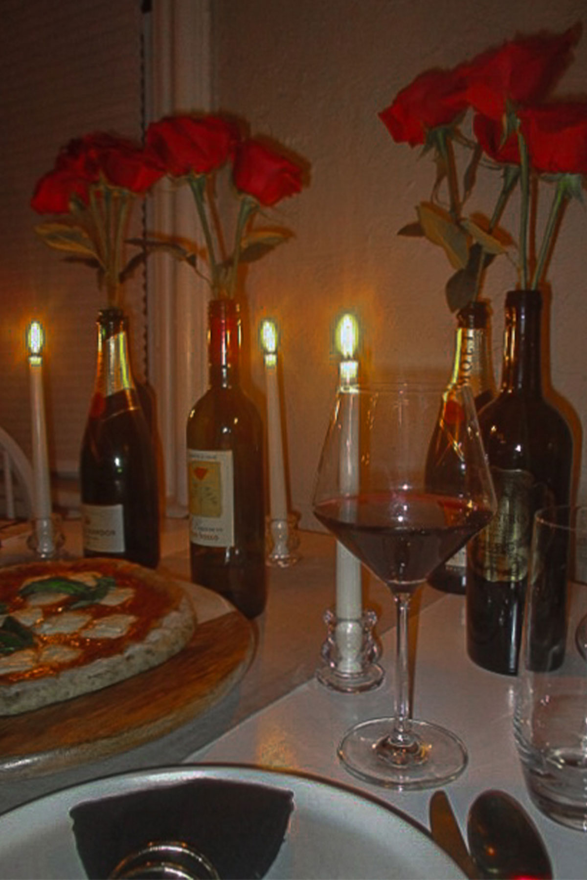 Valentine's Day dinner table with homemade pizza, red wine glass, candles and red rose arrangement