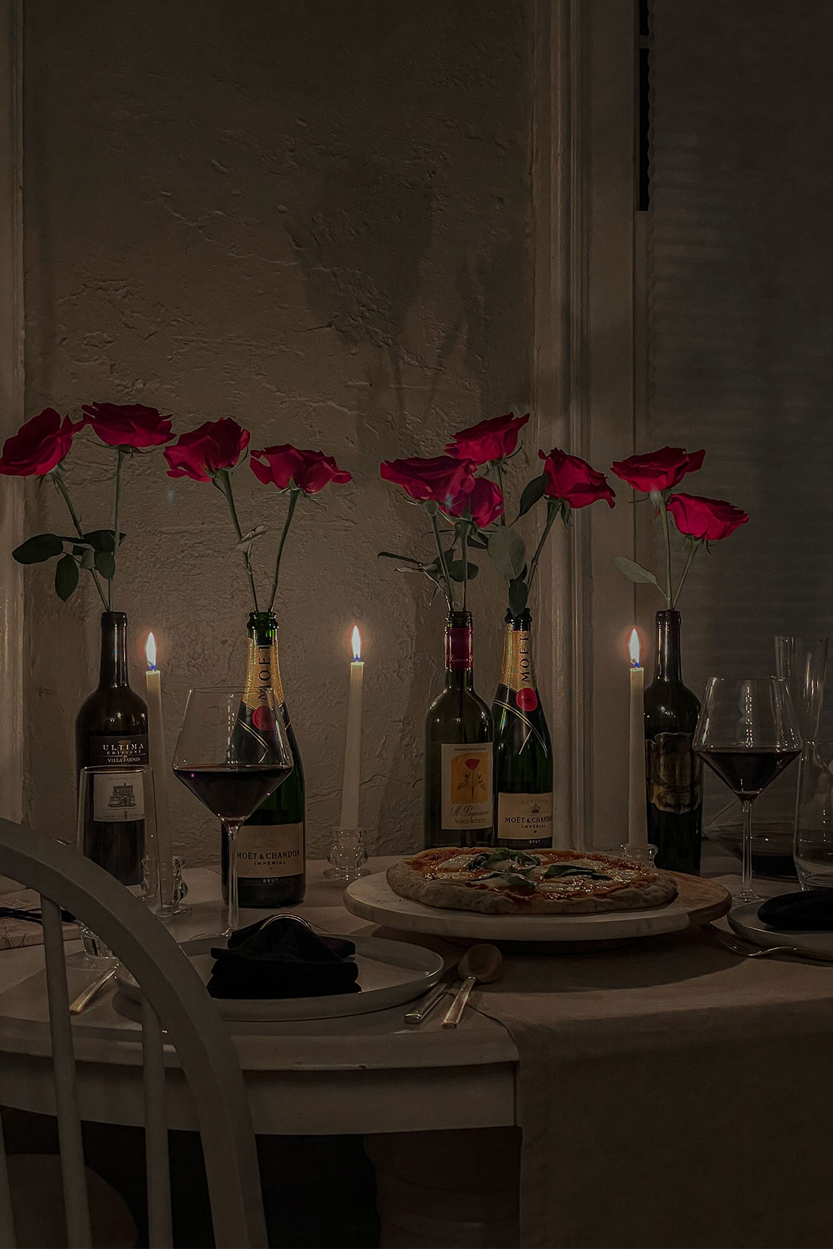 Valentine's Day dinner table with homemade pizza, glasses of red wine and wine bottles filled with red roses