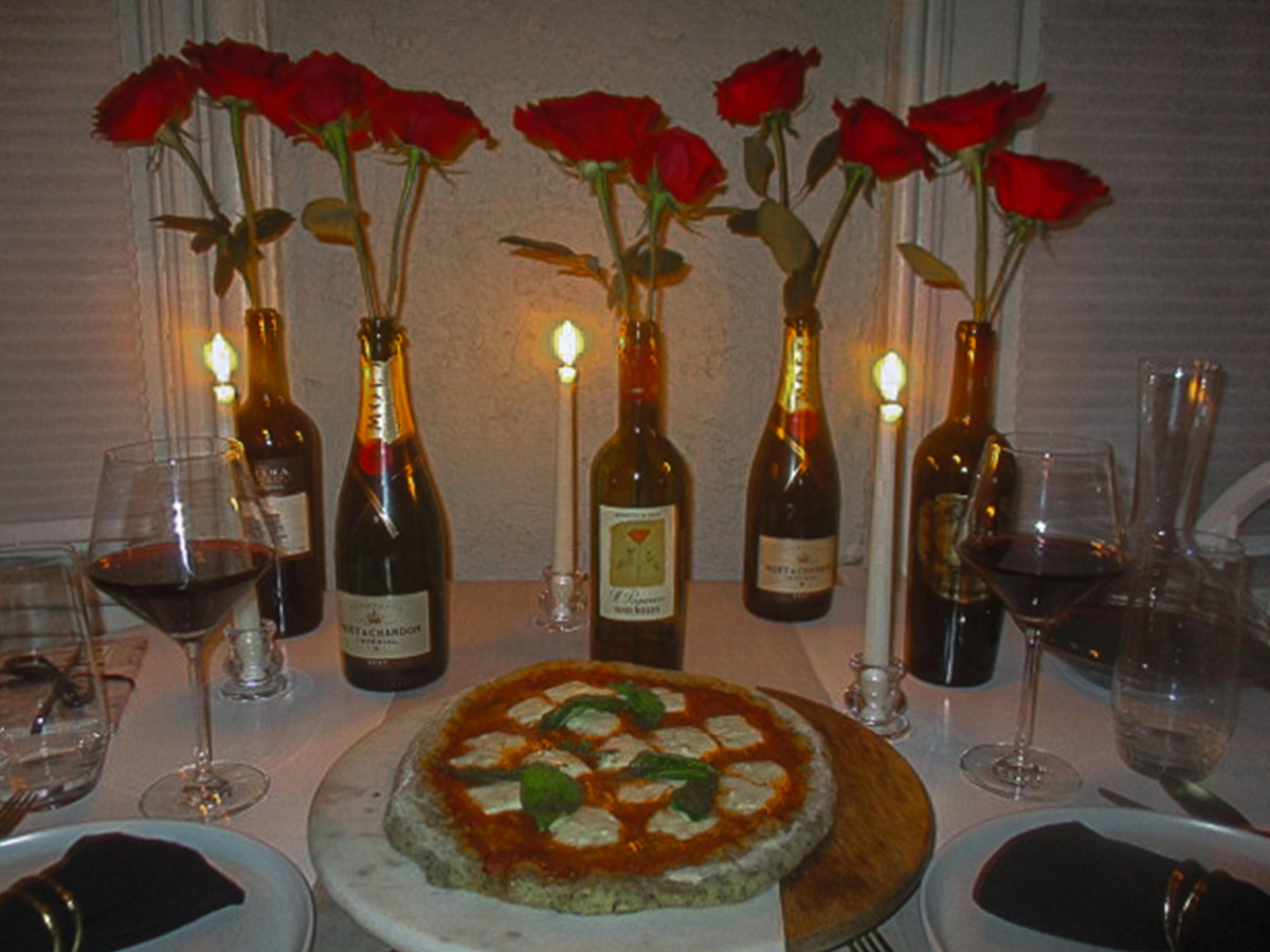 Valentine's Day dinner table with homemade pizza, glasses of red wine and wine bottles filled with red roses