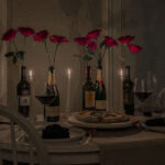 Valentine's Day dinner table with homemade pizza, glasses of red wine and wine bottles filled with red roses