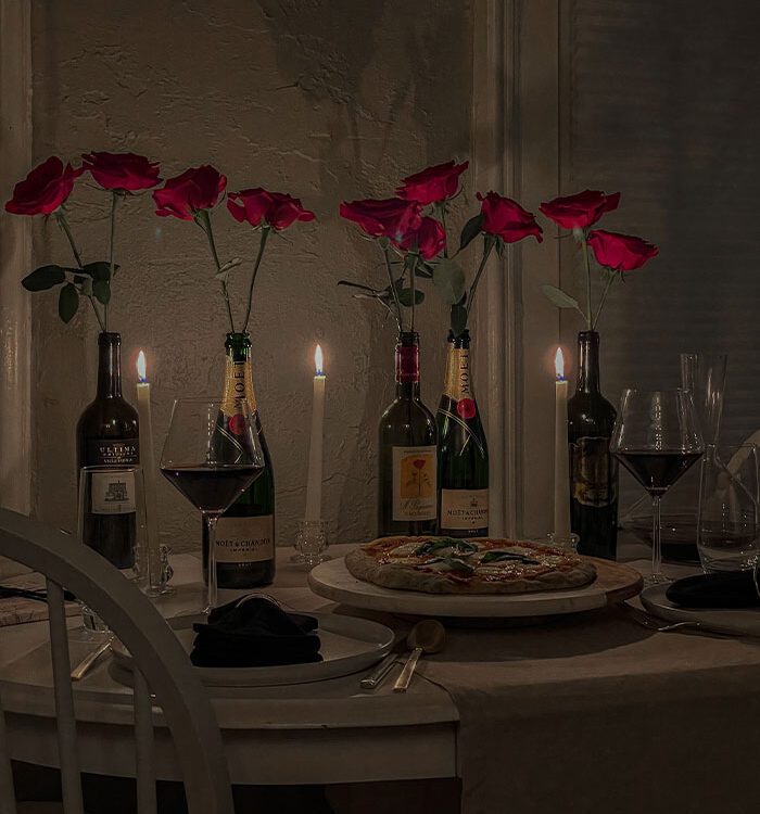 Valentine's Day dinner table with homemade pizza, glasses of red wine and wine bottles filled with red roses