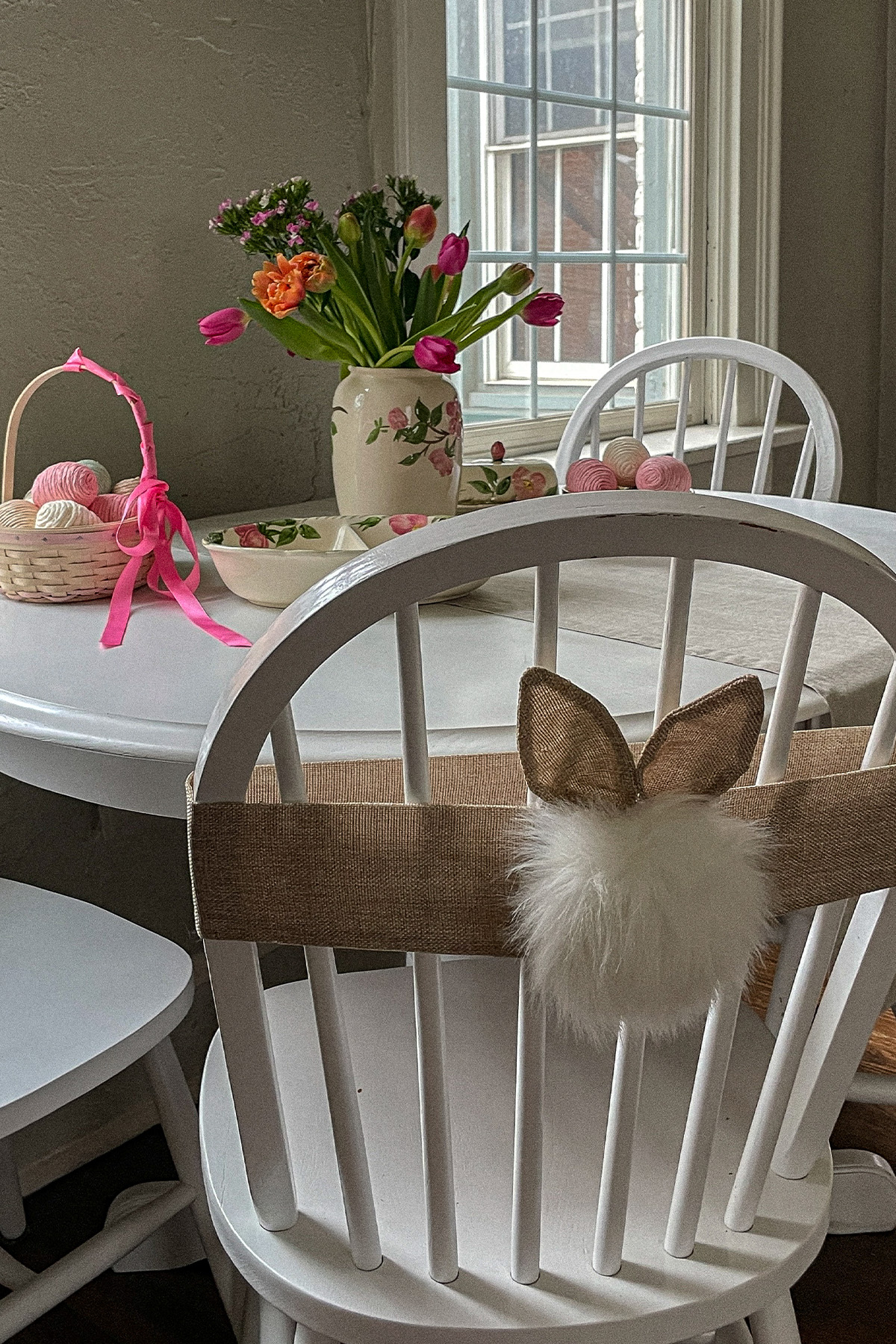 Decorative Easter table filled with spring flowers, an Easter basket with pastel eggs and bunny ears and cottontail attached to a chair