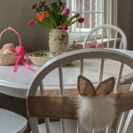 Decorative Easter table filled with spring flowers, an Easter basket with pastel eggs and bunny ears and cottontail attached to a chair