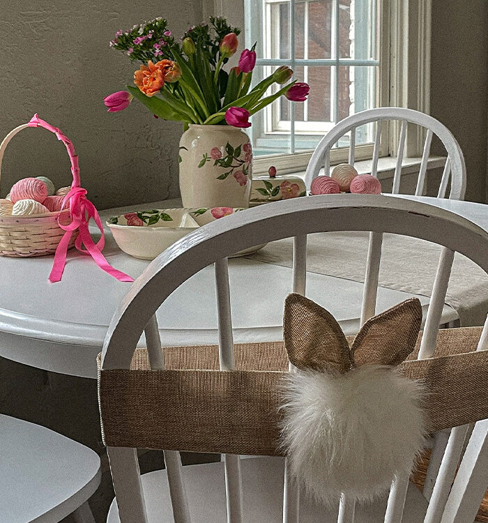 Decorative Easter table filled with spring flowers, an Easter basket with pastel eggs and bunny ears and cottontail attached to a chair