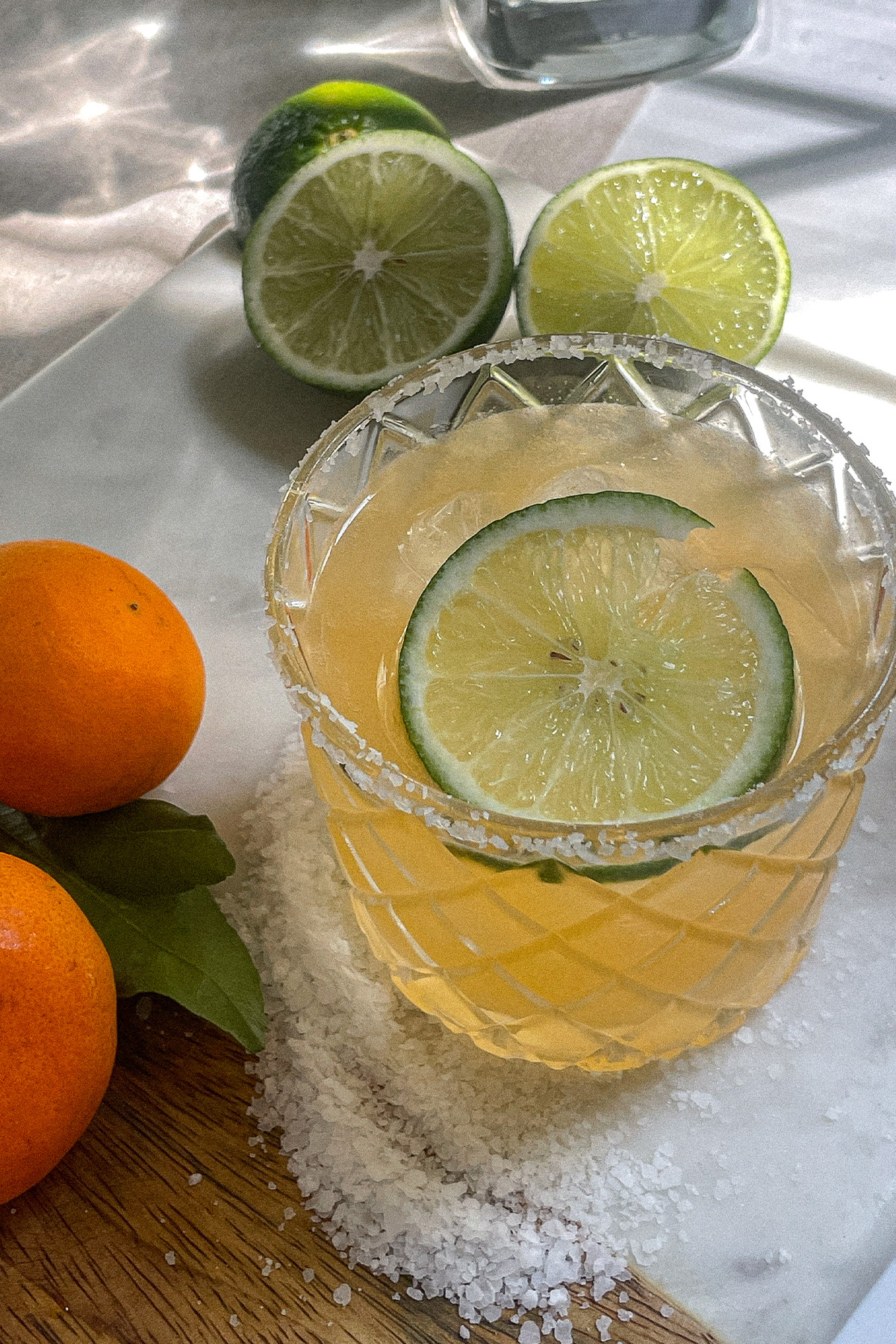 Mandarin orange margarita in a salt-rimmed glass surrounded by fresh oranges and limes