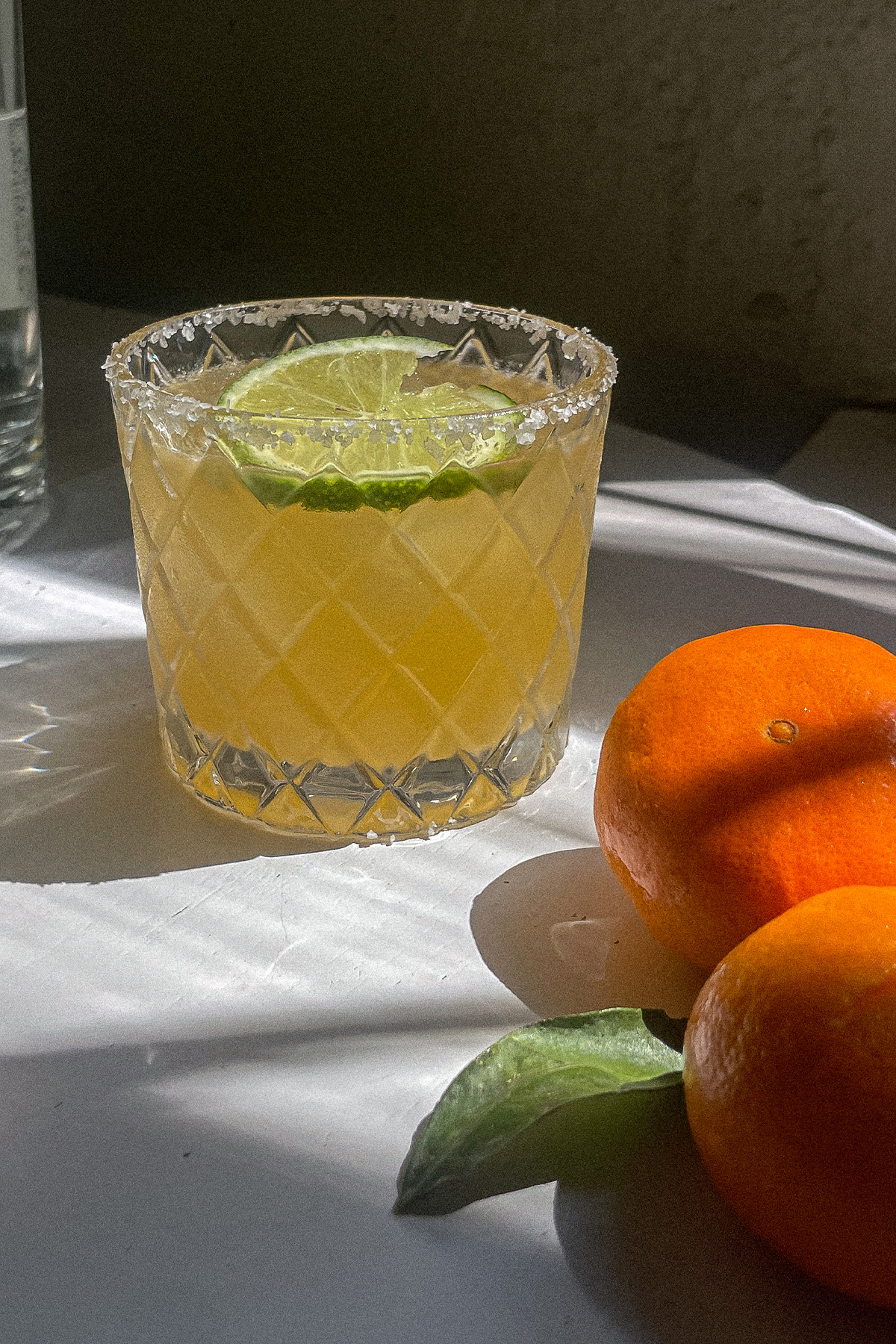 Mandarin orange margarita in a salt-rimmed glass surrounded by fresh oranges