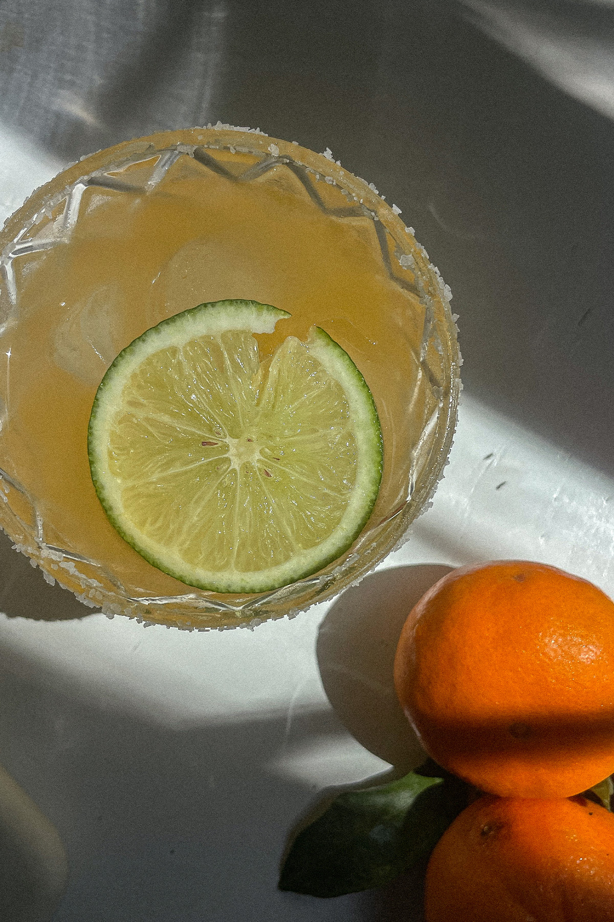 Mandarin orange margarita in a salt-rimmed glass surrounded by fresh oranges