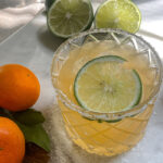 Mandarin orange margarita in a salt-rimmed glass surrounded by fresh oranges and limes