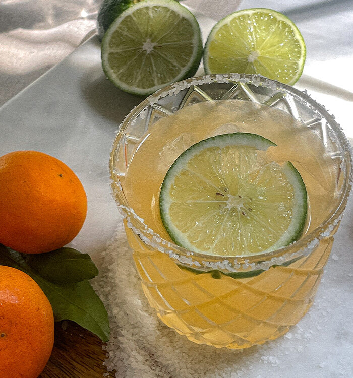 Mandarin orange margarita in a salt-rimmed glass surrounded by fresh oranges and limes