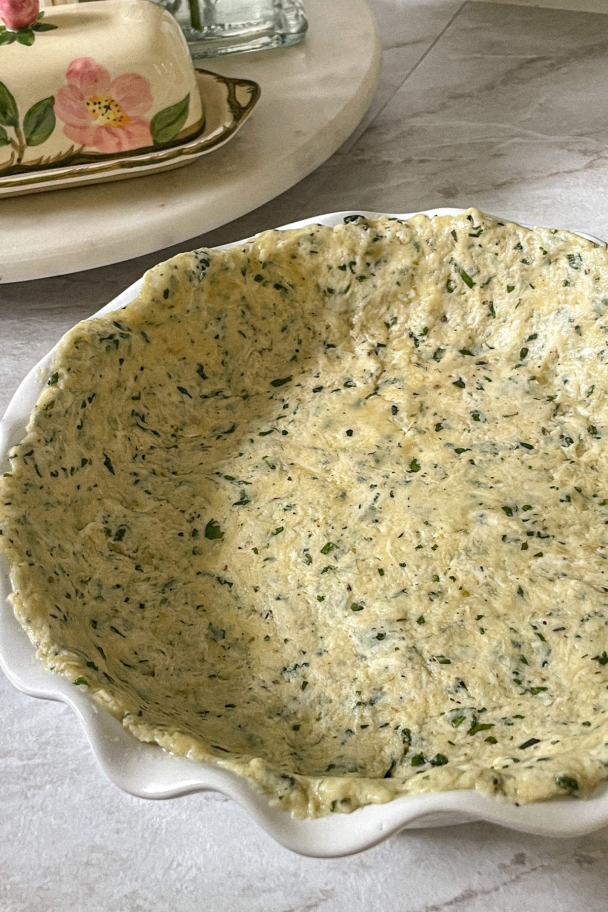 Homemade basil crust spread in a white ruffle pie pan