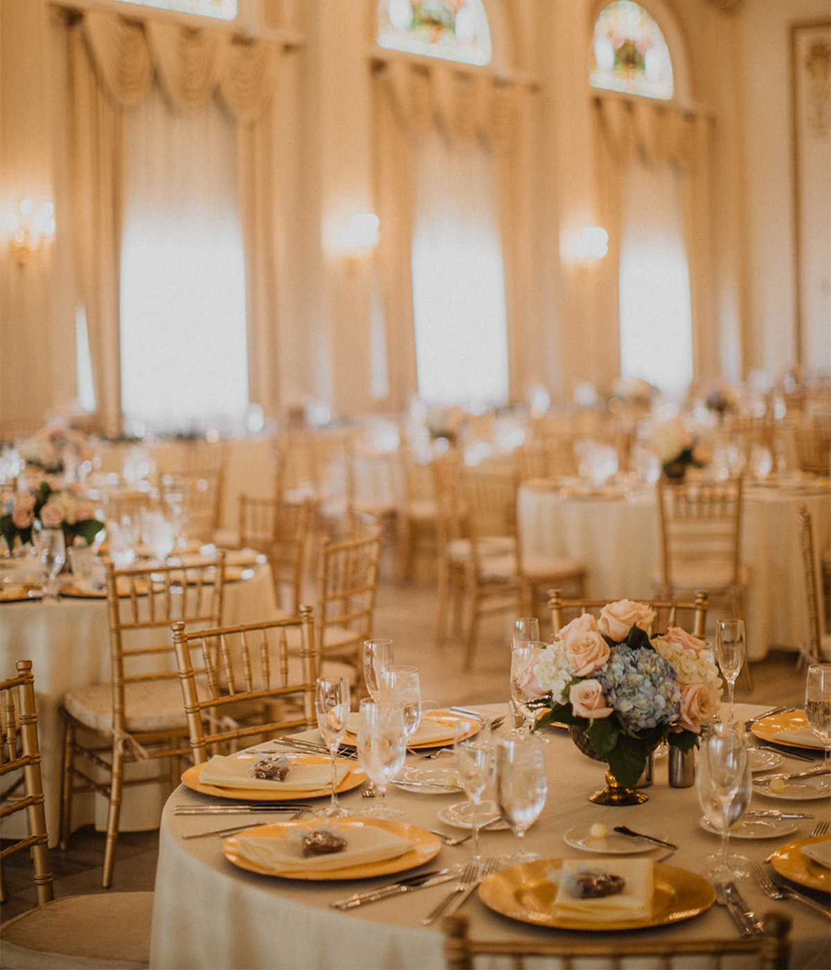 Gold ballroom wedding venue filled with set tables and gorgeous flowers