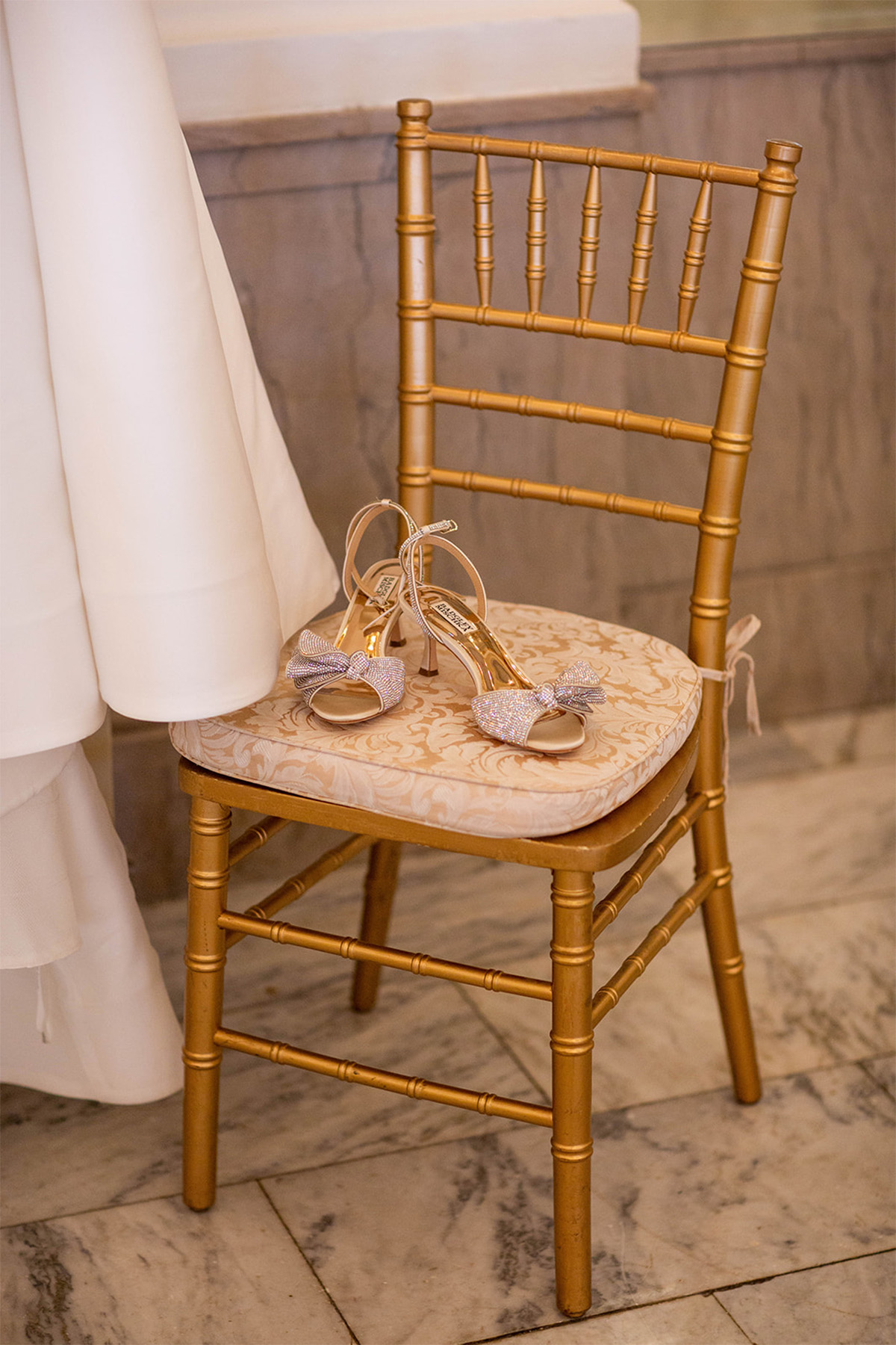 Bride's wedding shoes sitting on a gold chair next to her hanging dress