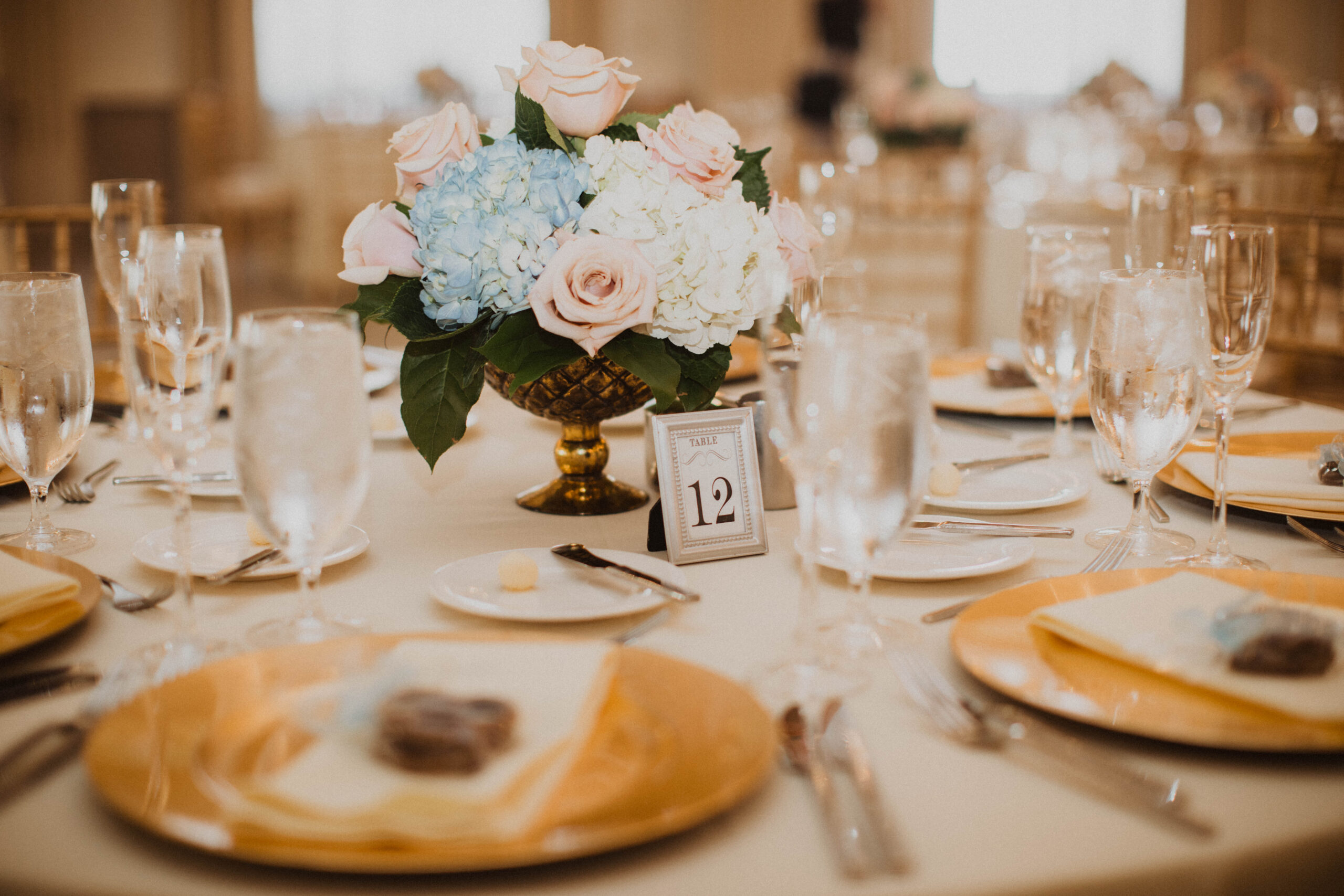 Beautiful wedding guest table set with gold chargers, sparkling glassware and flower arrangement