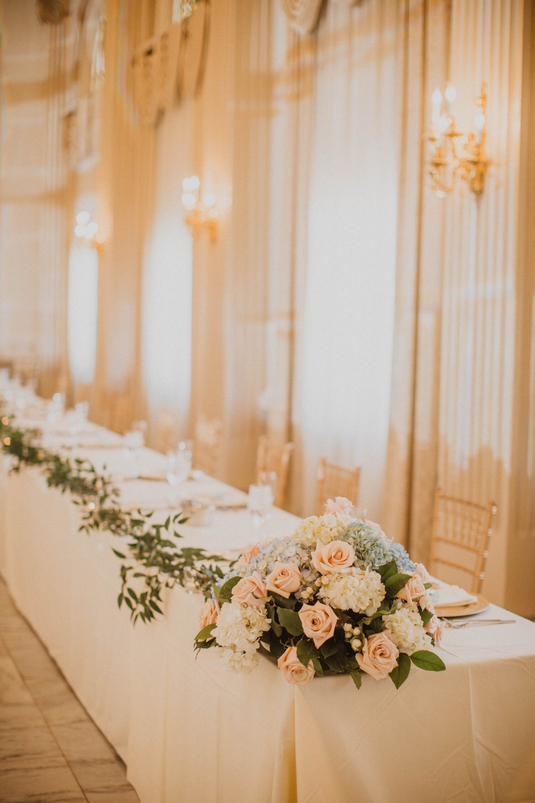 Beautiful wedding party table covered in blue and white hydrangeas, pink ranunculus and greenery