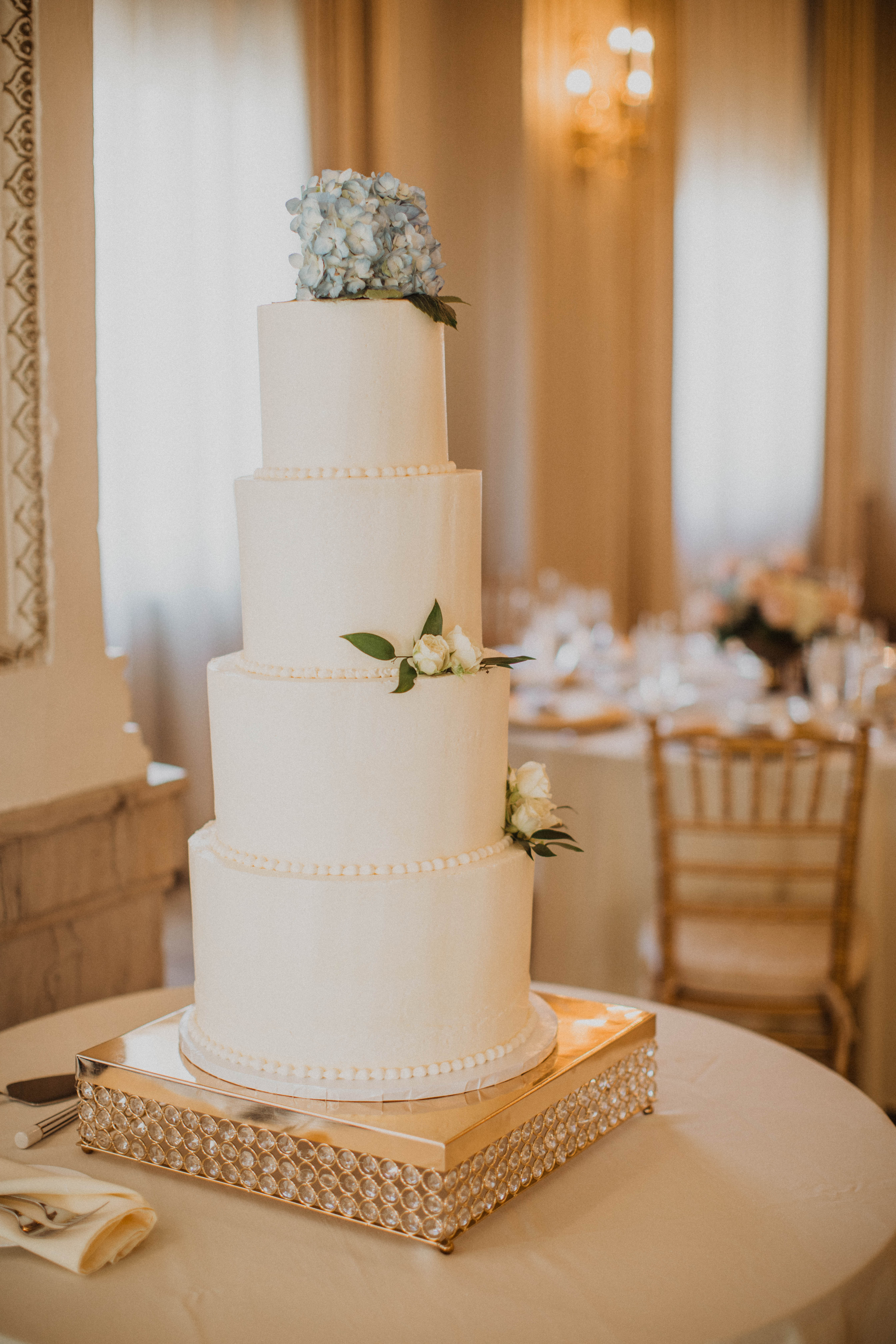 Simple four-tiered white wedding cake topped with blue hydrangeas