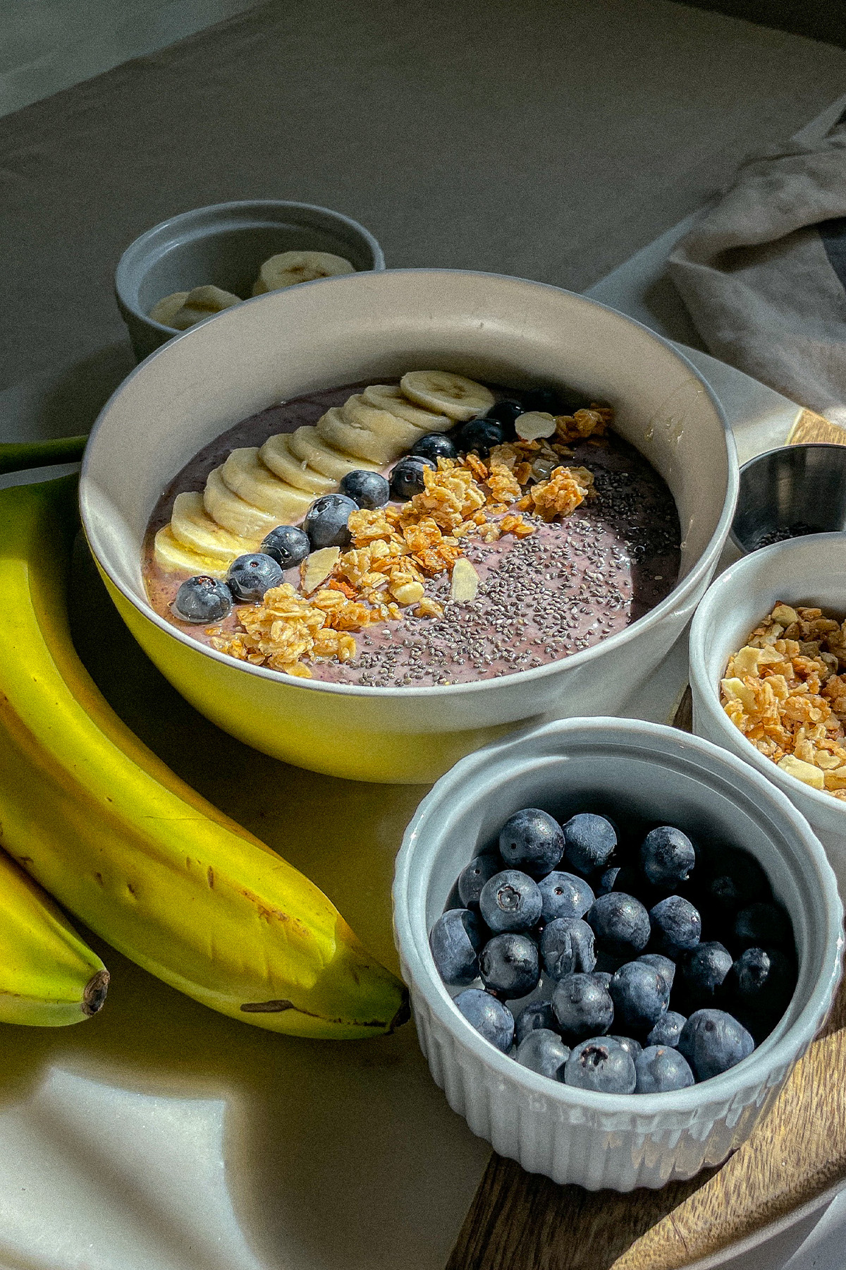 Blueberry Smoothie Bowl on a board with bowls of fresh fruit and granola