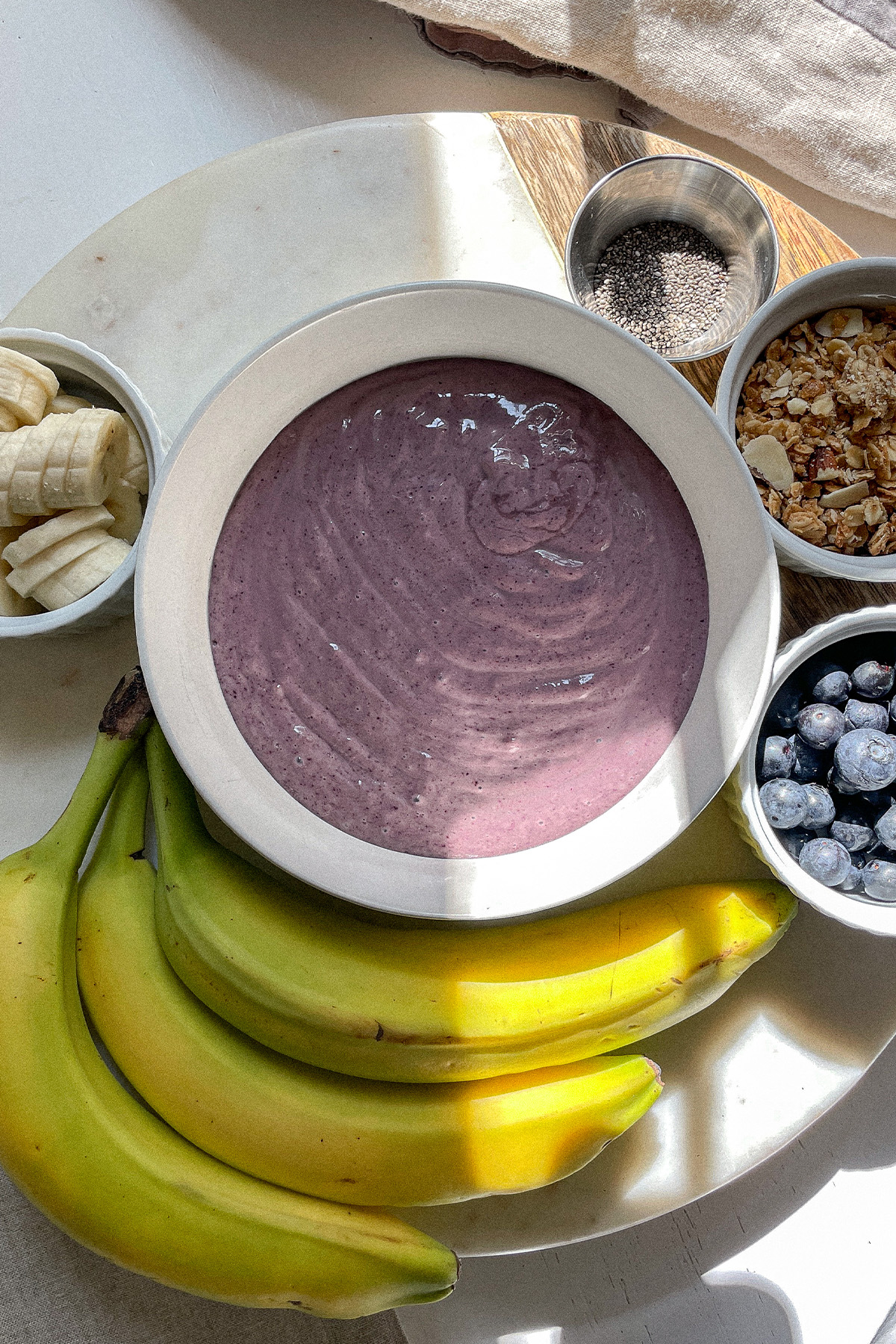 Blueberry Smoothie Bowl on a board with bowls of fresh fruit and granola ready to add