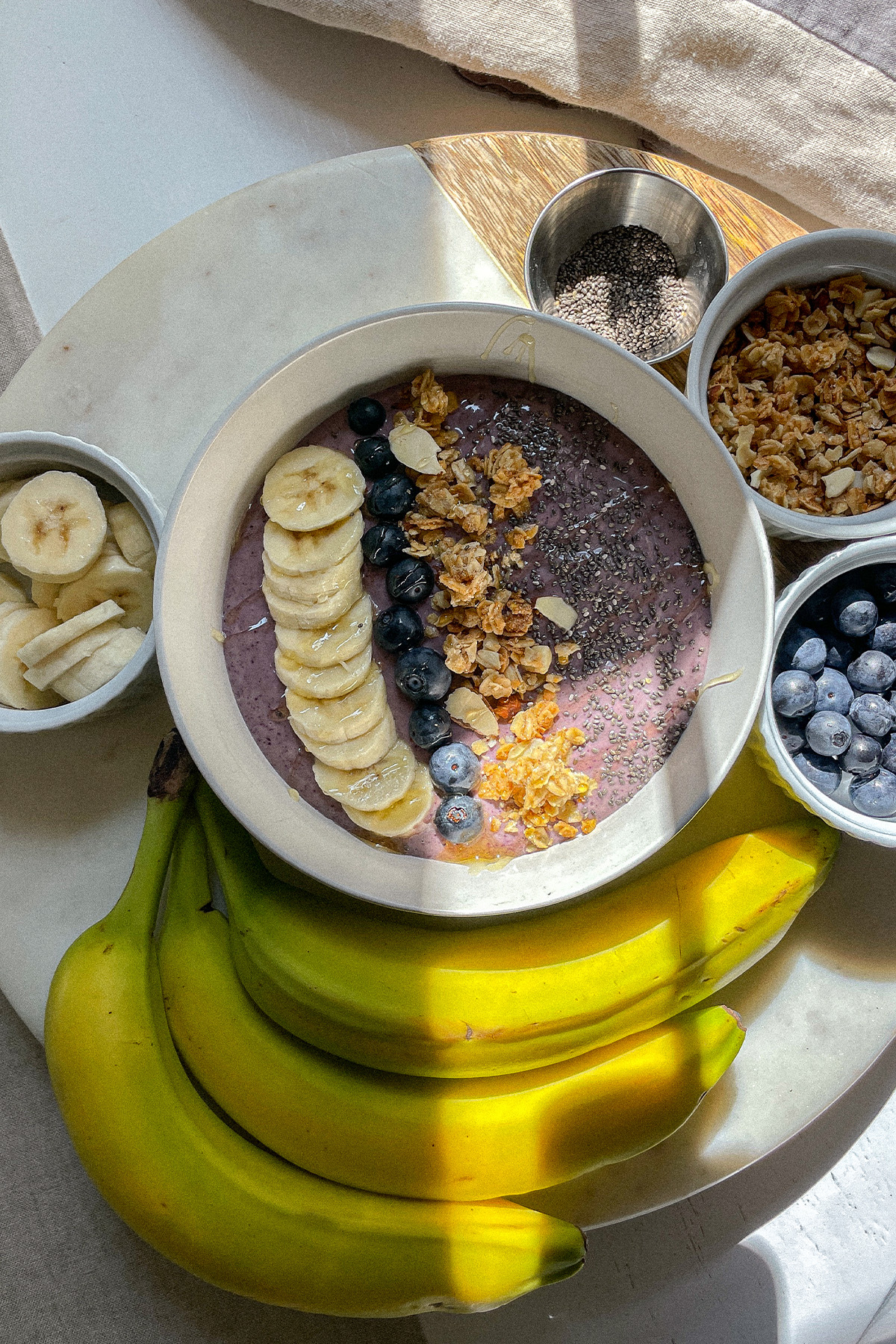 Blueberry Smoothie Bowl on a board with bowls of fresh fruit and granola