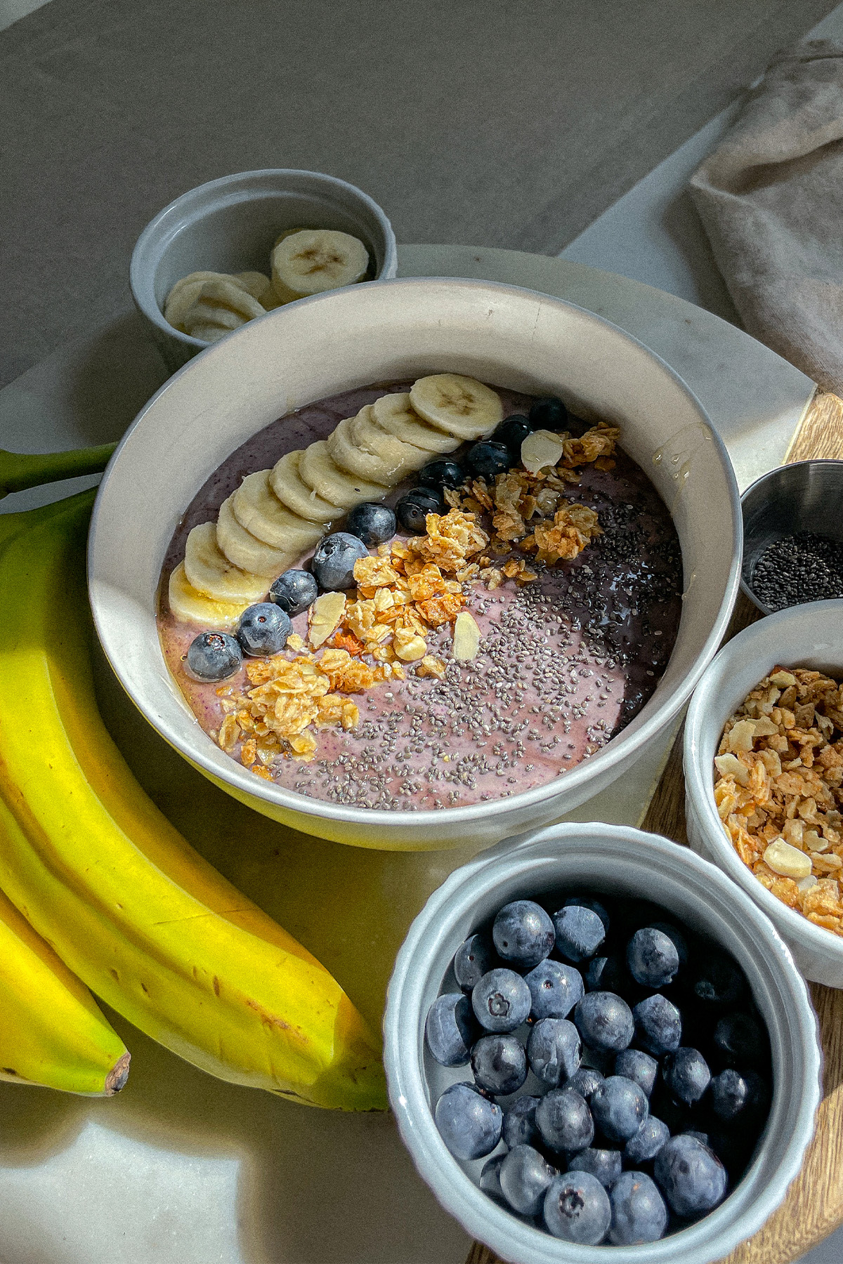 Blueberry Smoothie Bowl on a board with bowls of fresh fruit and granola