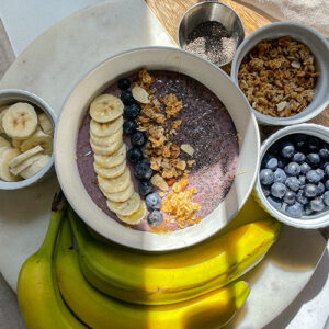 Blueberry Smoothie Bowl on a board with bowls of fresh fruit and granola