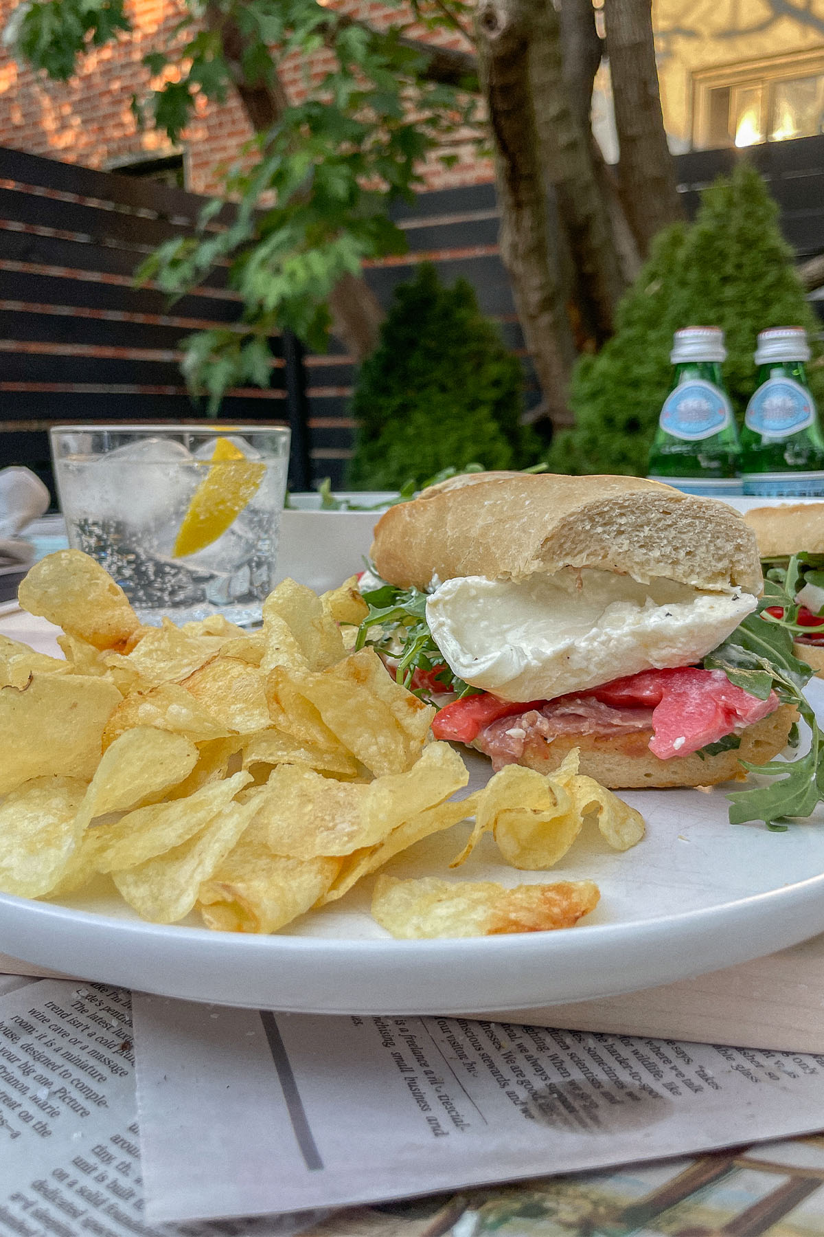 Prosciutto Burrata Baguette Sandwich half served on a plate with chips and a glass of Sanpellegrino with lemon