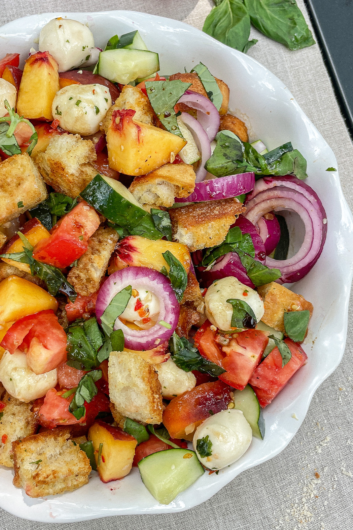 Colorful Peach Panzanella Salad in a white ruffle dish