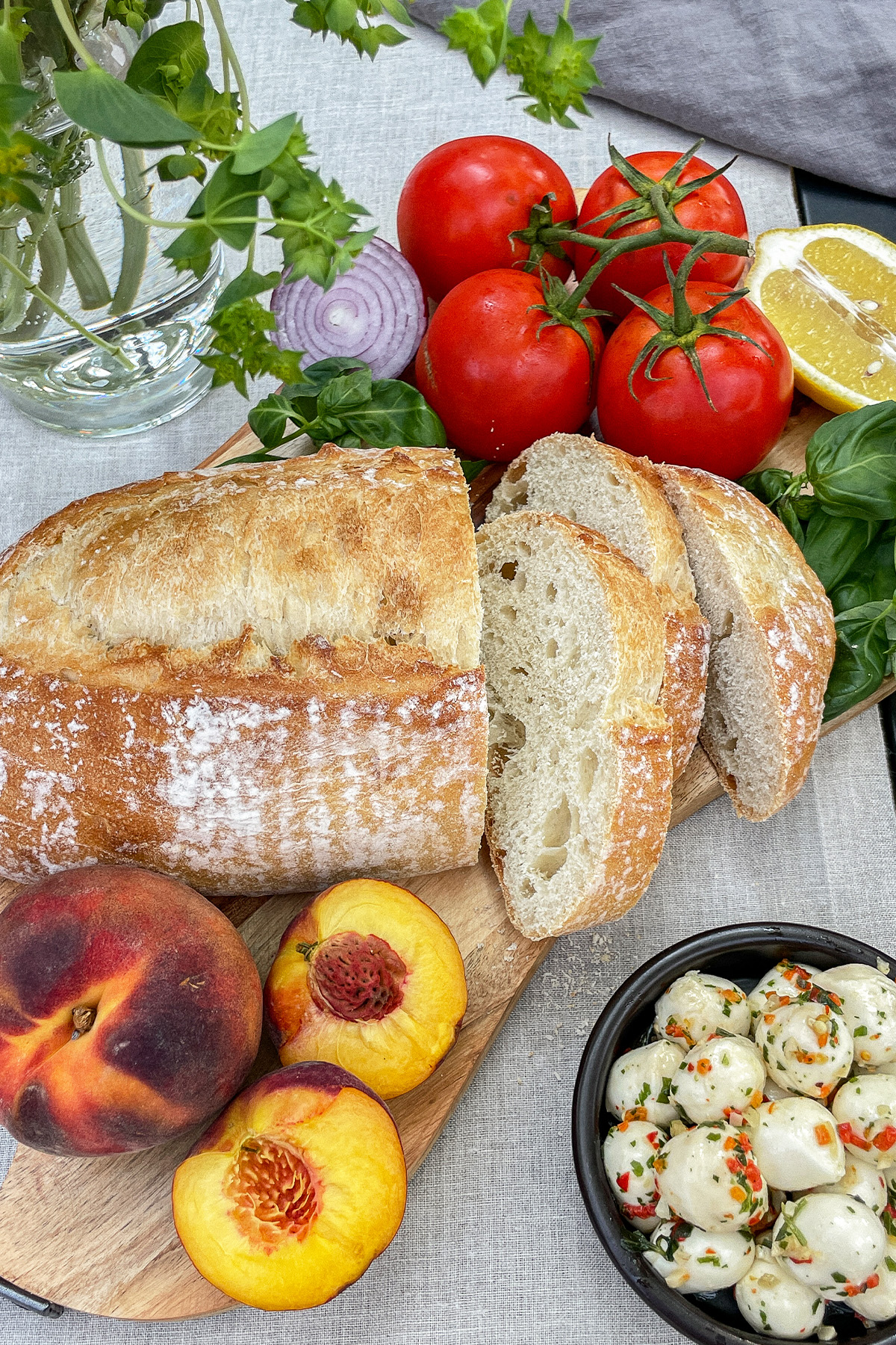 Sliced loaf of rustic Italian bread, fresh peaches, tomatoes on the vine, red onion, lemon and fresh mozzarella balls