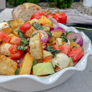 Colorful Peach Panzanella Salad in a white ruffle dish