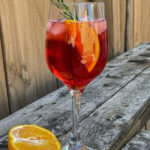 Cranberry Aperol Spritz served in a wine glass and garnished with an orange slice and rosemary sprig