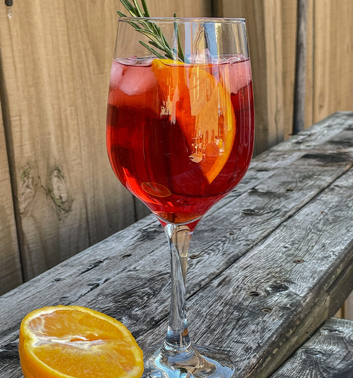 Cranberry Aperol Spritz served in a wine glass and garnished with an orange slice and rosemary sprig