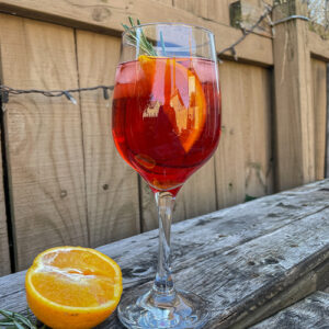 Cranberry Aperol Spritz served in a wine glass and garnished with an orange slice and rosemary sprig