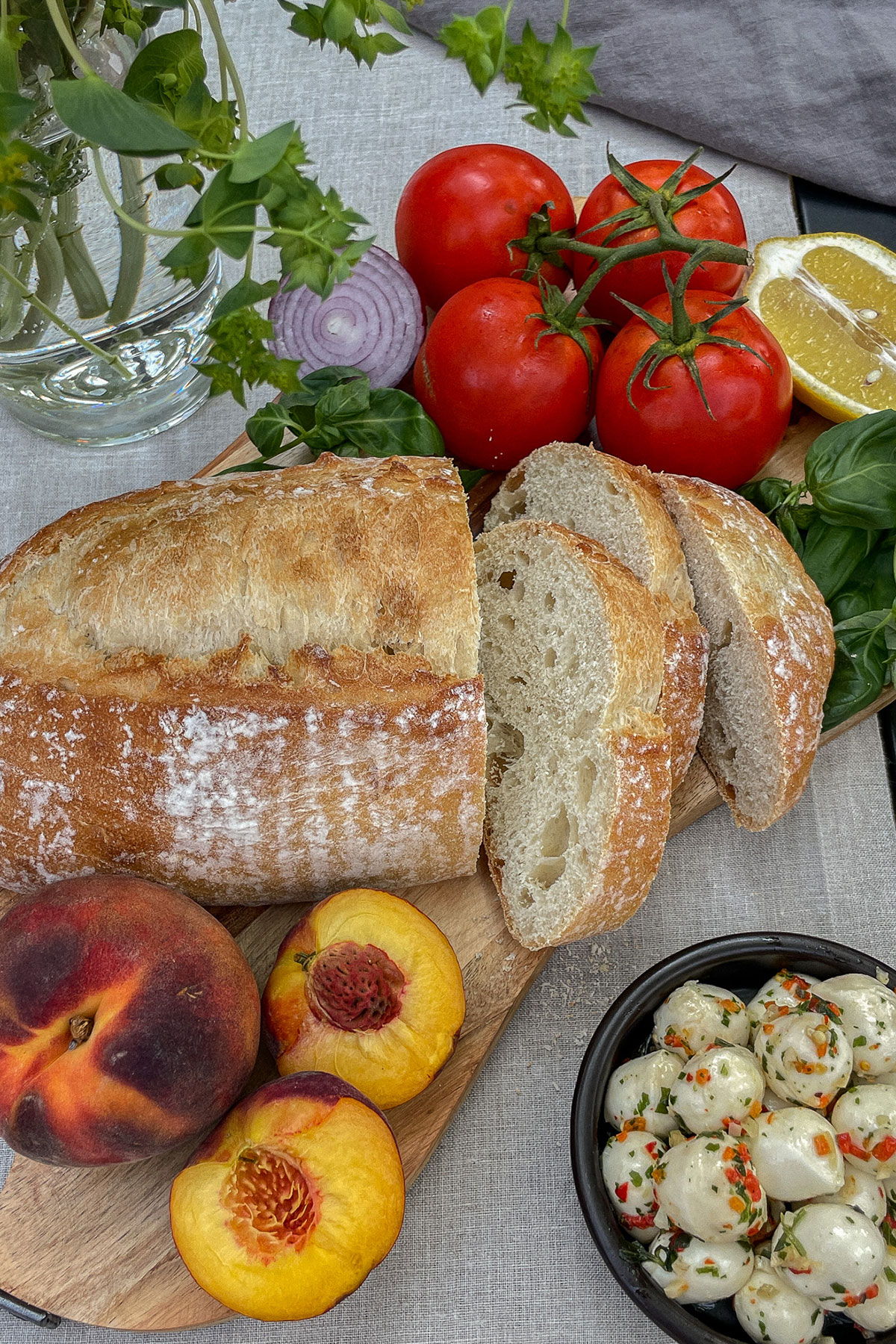 Sliced loaf of rustic Italian bread, fresh peaches, tomatoes on the vine, red onion, lemon and fresh mozzarella balls