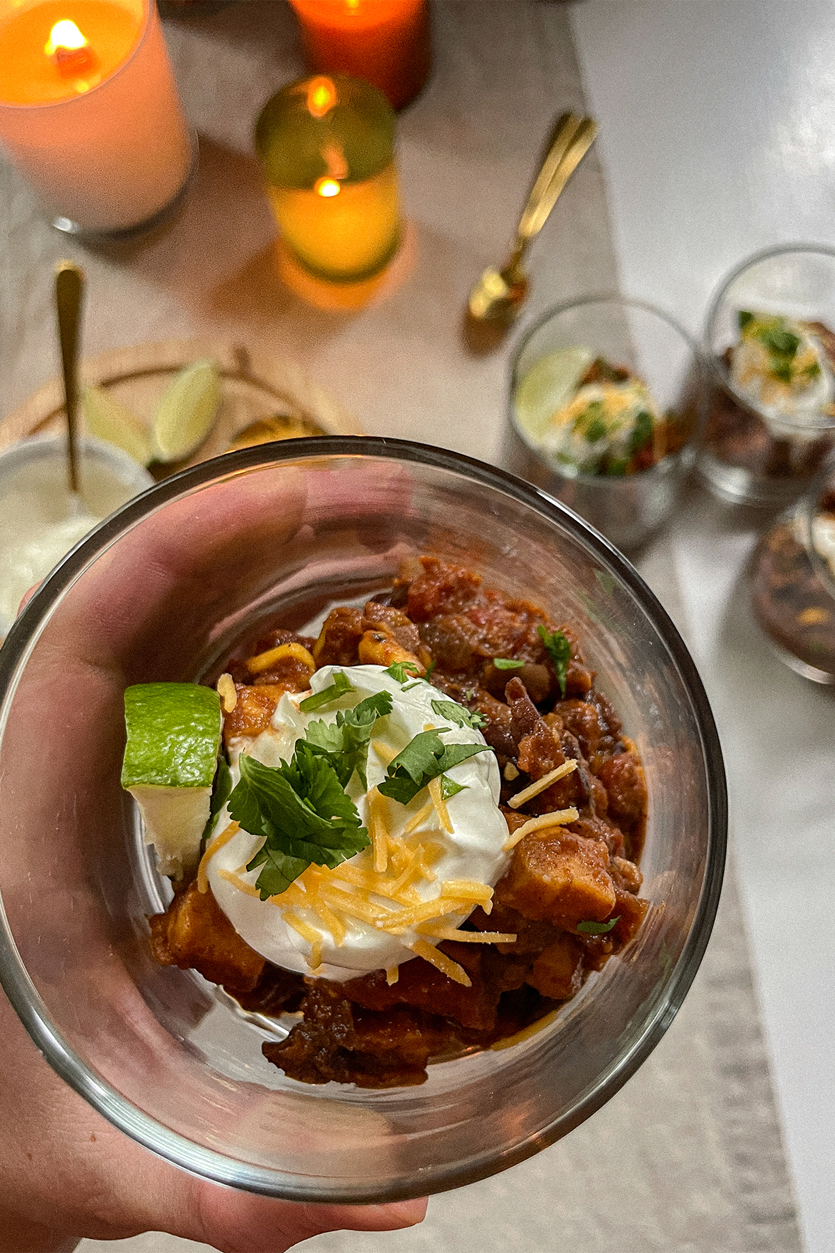 Southwest Sweet Potato Chili served in a glass cup topped with sour cream, cheese, cilantro and a lime wedge