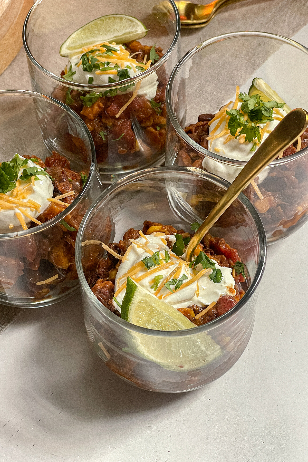 Southwest Sweet Potato Chili served in glass cups topped with sour cream, cheese, cilantro and a lime wedge