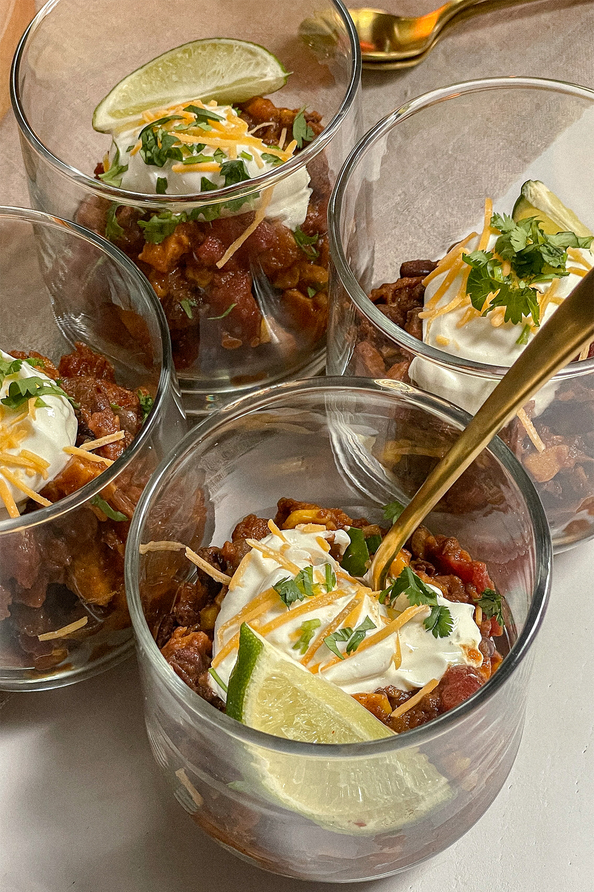 Southwest Sweet Potato Chili served in glass cups topped with sour cream, cheese, cilantro and a lime wedge