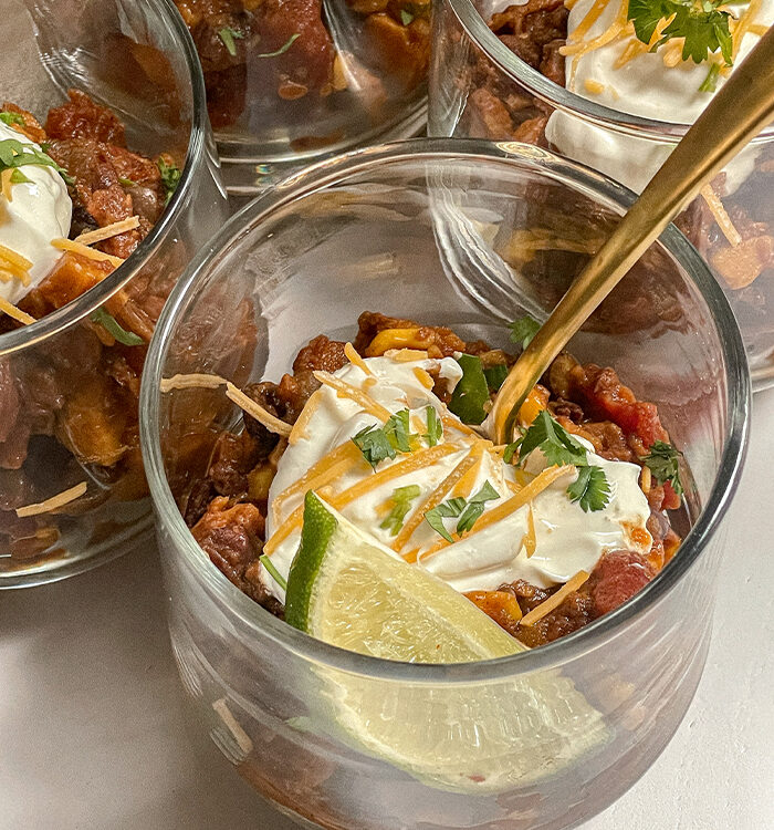 Southwest Sweet Potato Chili served in glass cups topped with sour cream, cheese, cilantro and a lime wedge